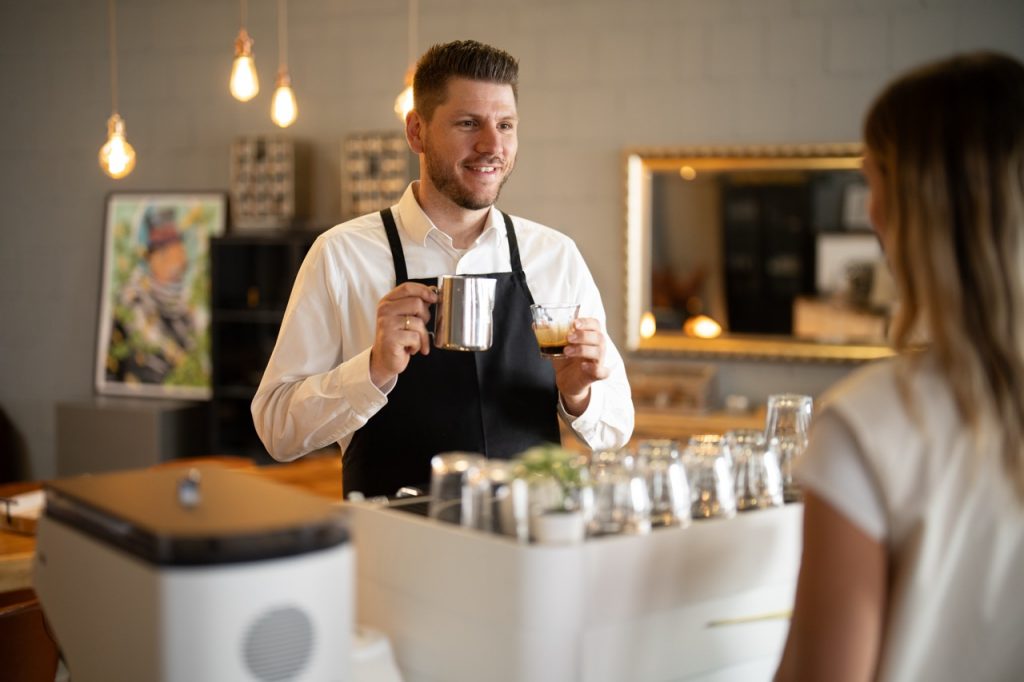 Barista vor mobiler Kaffeebar mit Espressoglas und Milchkanne
